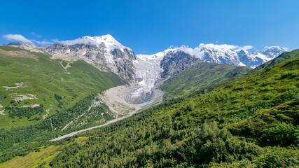 Naklejka premium A panoramic view on the snow-capped peaks of Tetnuldi, Gistola, Lakutsia and the Adishi Glacier in the Greater Caucasus Mountain Range in Georgia, Svaneti Region. Sharp peaks, wanderlust, solitude.
