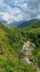 Fototapeta na wymiar A panoramic view on the cloud covered peaks of Tetnuldi, Gistola and Lakutsia in the Greater Caucasus Mountain Range in Georgia, Svaneti Region. River Adishischala flowing down the valley.