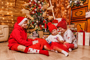 three cute children in red clothes open Christmas gifts sitting at the tree