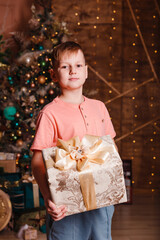 teenage boy holding a large box with a gift against the background of a Christmas tree