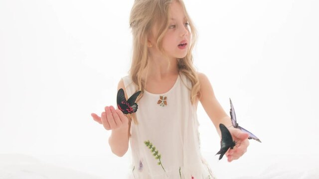 Beautiful little girl in a dress in the studio on a white background plays with real big butterflies.