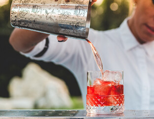 Caucasian beautiful blond bar woman preparing a negroni cocktail outdoors at sunset in a location...