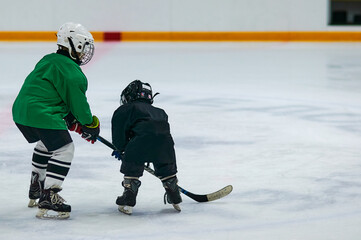 Two boys in hockey uniforms and protective helmets with hockey skates and a hockey stick standing on the ice of a large ice arena. Children in sports, young hockey players, champions concept.