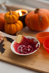 Mixing red icing sauce with a baking brush for halloween pumpkin muffins treats