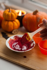 Mixing red icing sauce with a baking brush for halloween pumpkin muffins treats