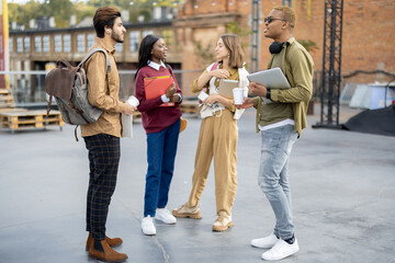 Obraz na płótnie Canvas Multiracial students standing and talking outdoors at day. Concept of education and learning. Idea of student lifestyle. Young modern guys and girls at university campus