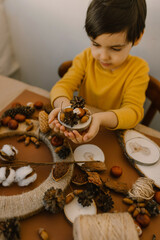 The boy makes a wreath from natural materials. Autumn needlework with handmade children