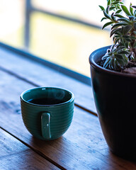 Vertical view of a steaming cup of coffee on a wooden table and a succulent plant on the right.