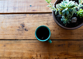 Top view of a coffee cup on a wooden table with a succulent plant on the side.