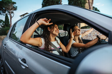Two young women sing a song on the radio and dance in the car on a day trip in the summer - Best...