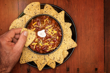 Hand dipping into a bowl of chili surrounded with chips