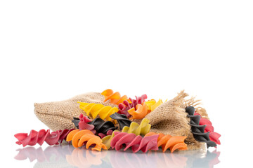 Uncooked colored fusilli pasta with jute bag, close-up, isolated on white.
