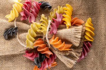 Raw colored fusilli pasta in a straw dish on sacking, close-up.