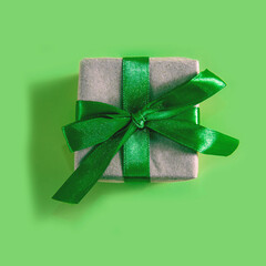 The above view on the present packed in the craft paper with the green satin ribbon on the green background. Minimalism New Year or Christmas concept.