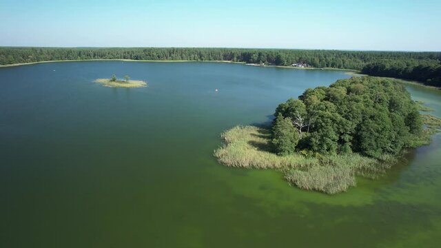 Slow drone flight low over the lake surrounded by the green forest. Small green islands in the middle of a shallow water.