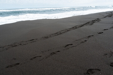 Traces on the black sand with the blue water of the sea in the background