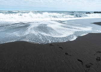 Human footprints in the black sand of pichilemu with view to the sea
