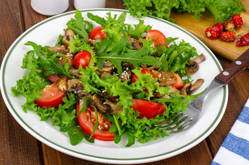 Diet salad of arugula leaves, tomatoes and fried mushrooms on wooden table. Studio Photo