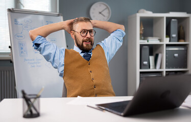 Fototapeta premium Happy bearded man in eyeglasses and stylish outfit working on wireless laptop while sitting at office. Caucasian businessman satisfied with success at work.