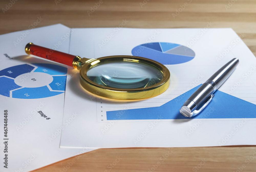 Poster magnifying lens on documents with business charts and graphs.