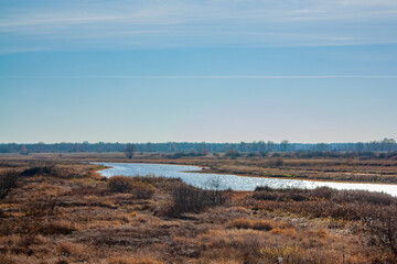 A small stream and yellowed autumn grass under a blue sky. Autumn landscape on a bright sunny day.