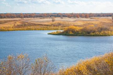 Autumn landscape on a bright sunny day. Yellow grass and bushes on the bank of the blue river.
