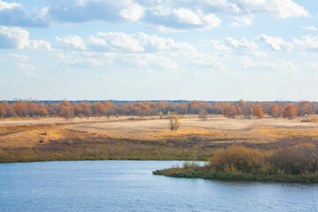 Autumn landscape on a bright sunny day. Yellow vegetation on the bank of the blue river.