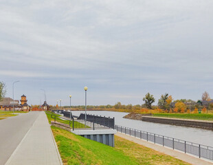 Autumn park with a pier and a beautiful shore. Sidewalk path on the river bank. A park with yellow and green trees.