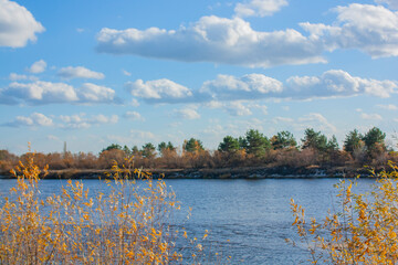 Beautiful clouds in the blue sky. Autumn landscape on a bright sunny day. Yellow and green trees on the bank of the blue river.