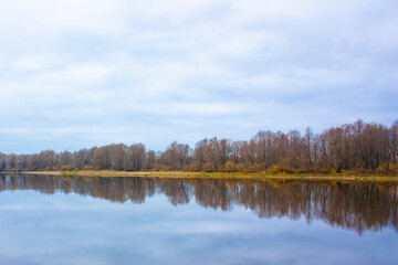 Obraz premium Reflection of the autumn forest on the smooth surface of the water. Autumn landscape of the opposite bank of the river in cloudy weather. 