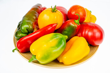 Arrangement of colorful fresh assorted bell peppers and tomatoes in wooden plate on white background. Studio Photo.