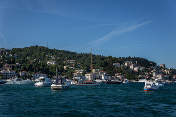 A beautiful Bosphorus shore view on a sunny day with lot of boats on the shore and houses over the green hills and a part of historic Rumeli castle in the back. 