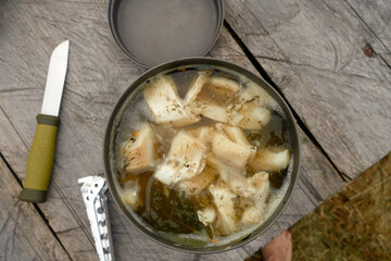 Fish soup in a metal plate on a wooden background. Cooking food on a tourist burner. Traditional...