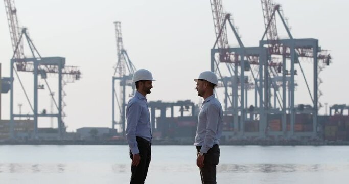 Engineers in protective helmets and formal shirts meet on berth to discuss work issues about portal cranes construction on foggy morning