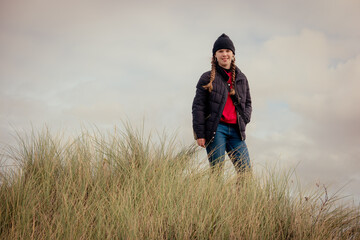 Naklejka na ściany i meble A teenage girl on a hike through nature and the coastal countryside in cold weather clothing