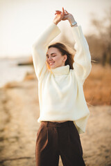 Portrait of a charming blonde with a gorgeous smile. A girl in a white sweater relaxes on the river bank