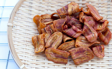 Banana slice chips in round bamboo basket on white background.