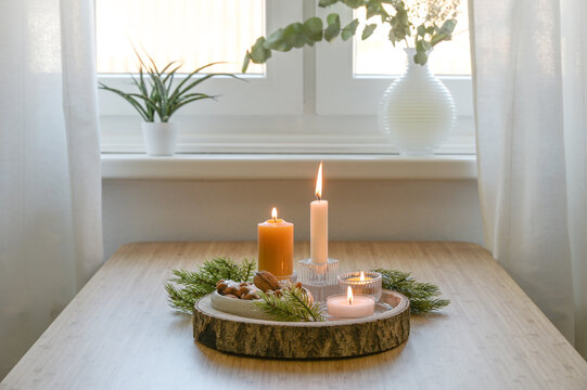 Advent and Christmas decoration, four different lit candles on a rustic wooden tray with fir branches and cookies on a table at the window, copy space