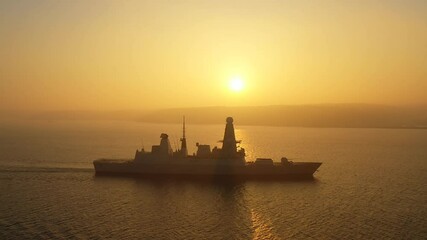 A modern air defence guided missile destroyer underway against the sun in mist