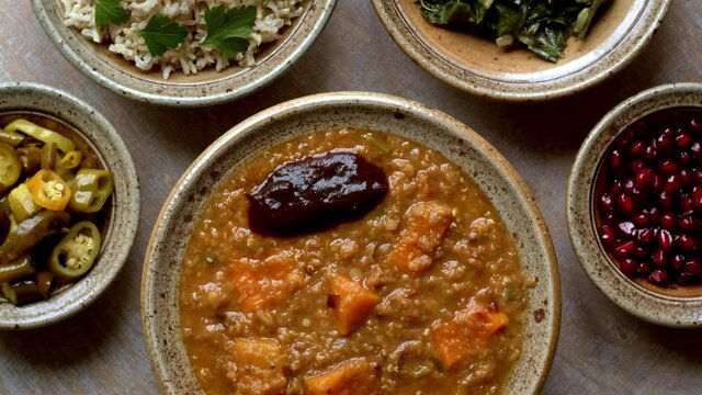 Red lentil, pumpkin and tamarind paste dish with sides in ceramic bowls. Top view table spin.