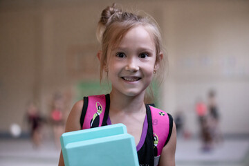 Portrait of smiling girl gymnast with fitness blocks and backpack in gym on training