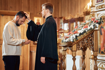 a priest blesses a bearded man in an Orthodox church after a festive church mass - obrazy, fototapety, plakaty