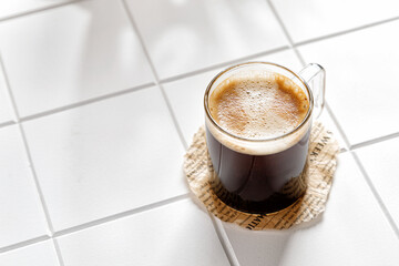 one espresso coffee in a glass mug on a white background with a tile