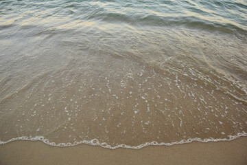 A small sea wave rolls over the sandy beach with clear water