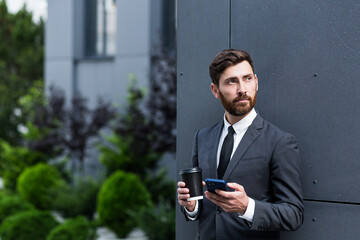 Successful businessman broker in a business suit talking on the phone near the office outside,...