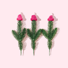 Three fir branches with pink caps with white pompom. Pastel pink background. Winter holidays in...