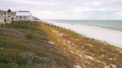 People walking on shore by wooden boardwalk stairs steps from waterfront oceanfront houses home properties at Santa Rosa Beach Seaside, Florida panhandle town by coast shore