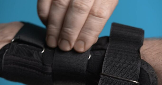 A man unfastens the straps of a wrist orthosis. Close-up.