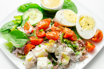 Healthy salad, potato salad with hard boiled egg, shredded ham, cucumber, tomatoes, lettuce and spinach with a honey and mustard dressing pot