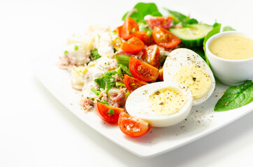 Healthy salad, potato salad with hard boiled egg, shredded ham, cucumber, tomatoes, lettuce and spinach with a honey and mustard dressing pot